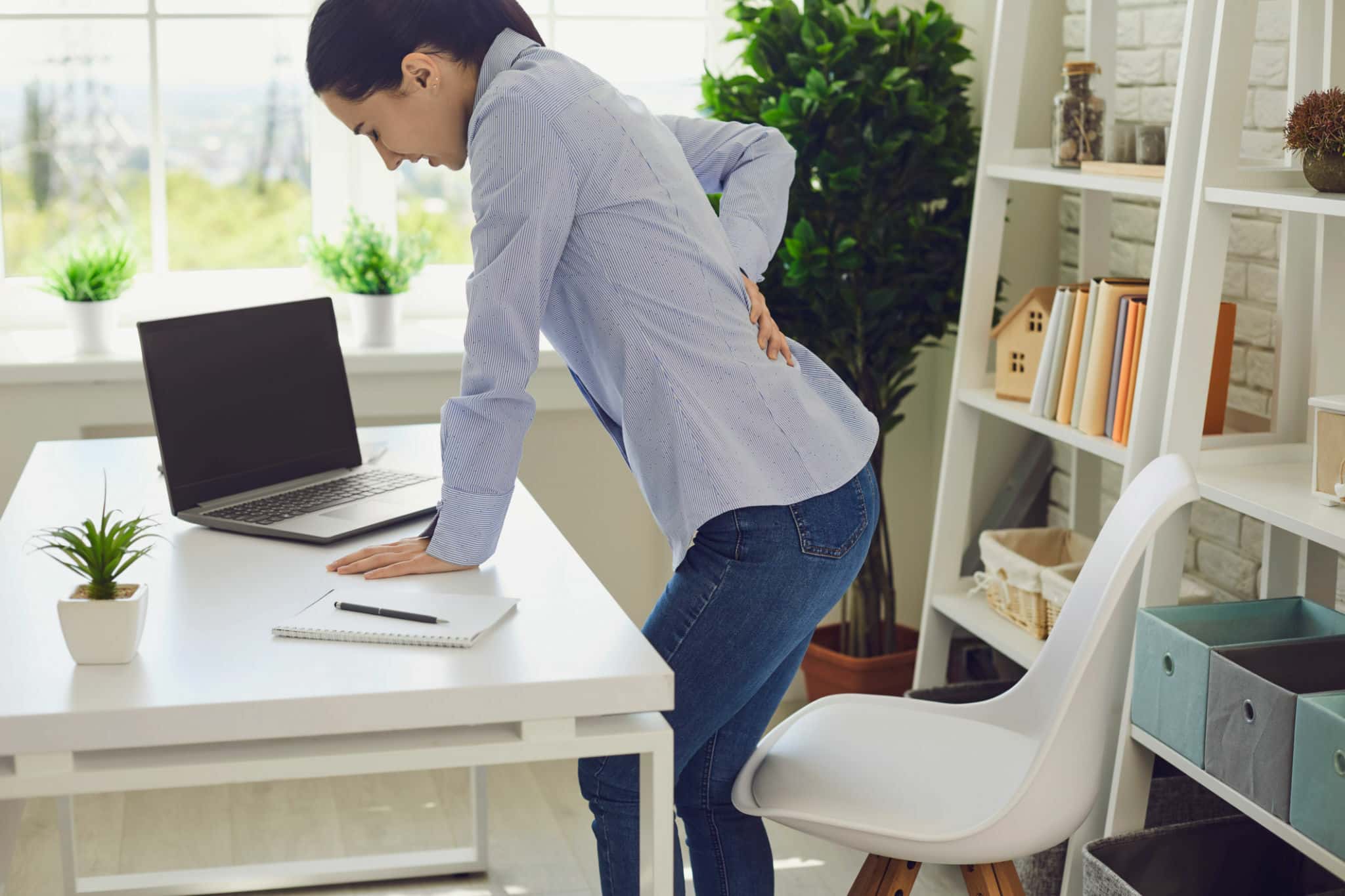 una mujer se apoya en el escritorio y se toma la espalda debido al dolor de ciática